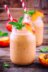 Two glass jars filled with peach smoothies and mint leaves, garnished with peach slices and red and white striped straws.